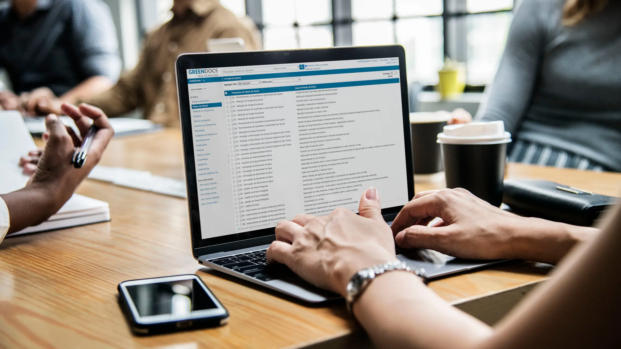 Trabalho em equipe em um escritório moderno, com pessoas utilizando laptops e tomando café, simbolizando produtividade e colaboração.