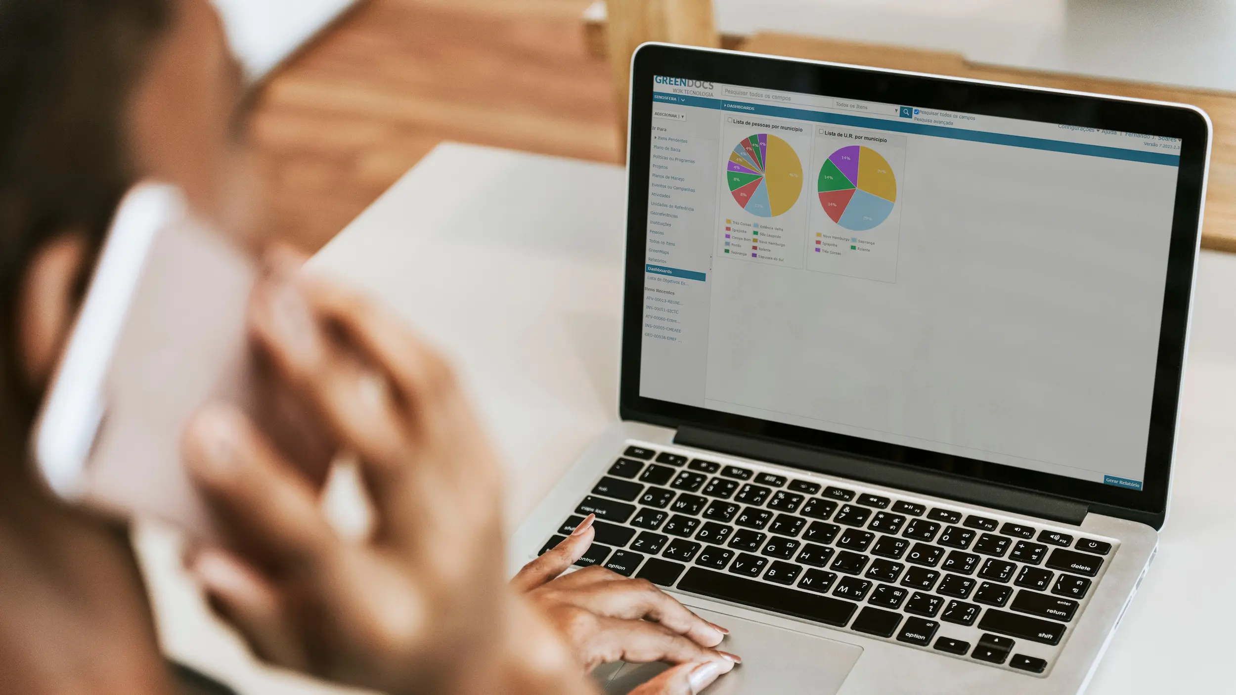 Pessoa usando laptop para visualização de gráficos e análise de dados, enquanto fala ao telefone, representando a integração de tecnologia e comunicação no trabalho.