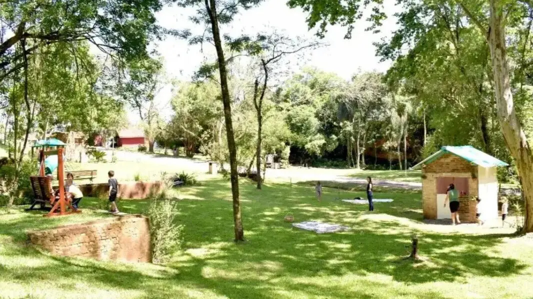 Parque ao ar livre com áreas verdes, crianças brincando, e um quiosque de madeira. Ideal para atividades recreativas e lazer em família.