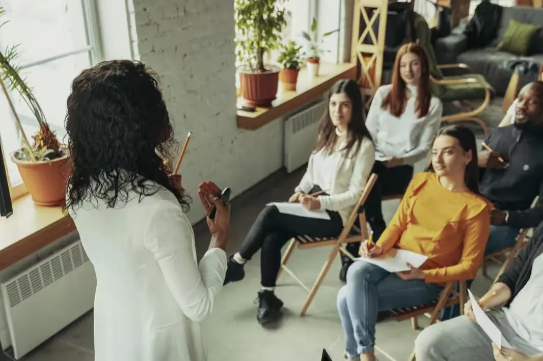 Aula interativa com um grupo diversificado de pessoas em um ambiente moderno e iluminado, aprendendo. O instrutor se destaca, gesticulando e compartilhando conhecimento.