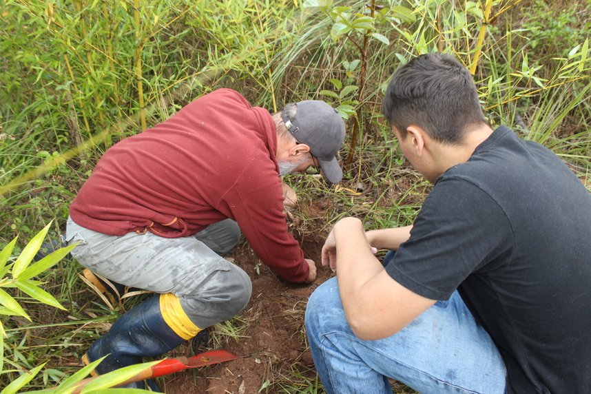 Dois homens em um campo, envolvidos em atividades de cultivo, com foco em plantio e trabalho com a terra em um ambiente natural.